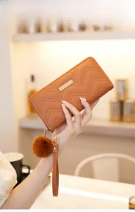 Close-up of orange long wave-quilted wallet with gold plate and pompom detail
