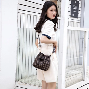 Classic checkered drawstring bucket bag with a wide strap shown in an outdoor casual setting