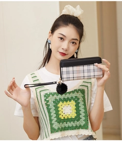 Women's long plaid wallet with black faux fur pompom and detachable wrist strap held by model