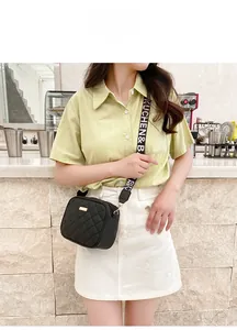Close-up of quilted black crossbody bag with wide logo strap worn by a model