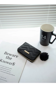 Detail of black quilted short wallet with gold bar and fluffy pompom keychain