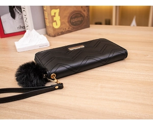 Detail of black wave quilted long wallet with gold metal plate and faux fur pompom charm