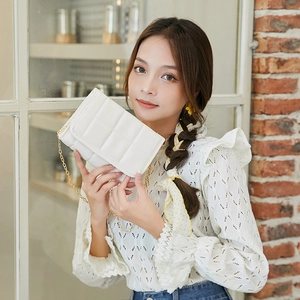 Elegant white quilted crossbody bag with gold chain strap shown against a brick wall