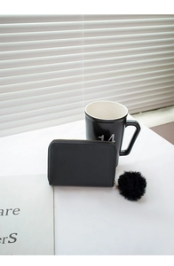 Close-up of black short wallet with wave stitching and a fluffy pompom keychain