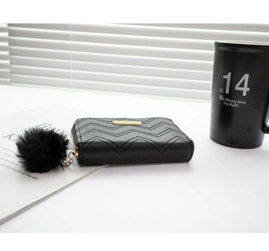 Detail of black wave quilted short wallet featuring gold nameplate and plush pompom charm