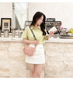 Pink quilted crossbody bag detail with wide lettered strap in a stylish cafe setting