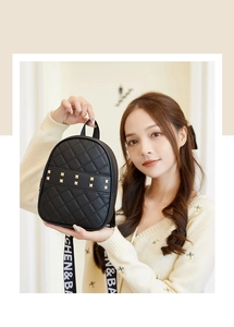 Close-up of small black quilted backpack with gold square rivets and brand letter strap
