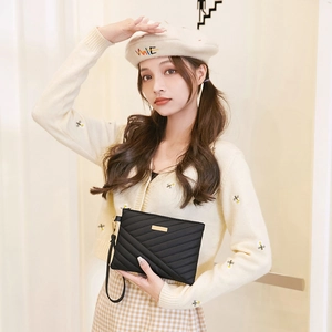 Pochette noire chic à matelassage en V avec détails dorés portée par un mannequin