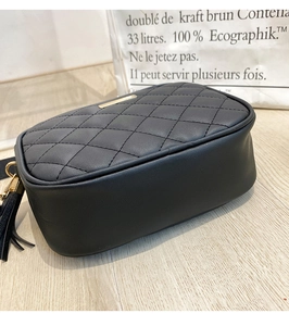Detailed side view of black quilted faux leather crossbody bag with tassel and gold plate