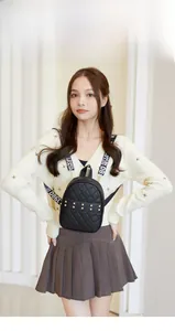 Model wearing a black quilted mini backpack with gold studs and lettered wide straps