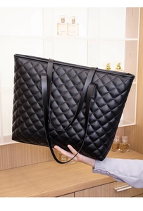 Detail of black quilted tote bag with refined diamond stitching held by model