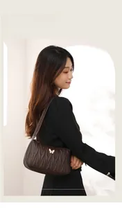 Detail of a dark brown quilted shoulder bag with gold butterfly logo on a female model