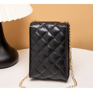 Detail of a black quilted leather crossbody bag with gold chain strap on a white table