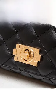 Close-up of golden metal twist lock and black quilted rhombus pattern on a chain bag