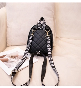 Detail of black quilted mini backpack featuring wide lettered straps and gold metal hooks