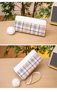 Detailed view of checkered wallet with white leather trim, wrist strap and pompom charm
