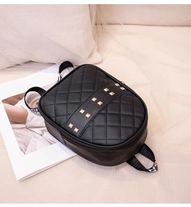 Detail of black quilted crossbody bag featuring golden studs and wide fabric strap