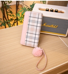 Detailed view of pink plaid wallet with furry pompom charm and wristlet on wooden table