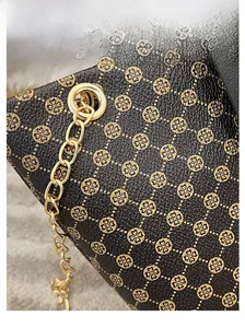 Macro shot of black textured leather bucket bag with gold clover pattern and metal chain