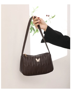 Detail of coffee shoulder bag featuring quilted texture and butterfly metal buckle