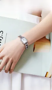 Détail d'une montre carrée argentée de luxe avec lunette en strass et bracelet chaîne