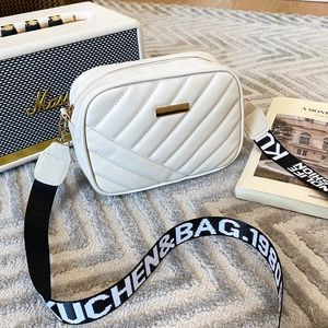 Quilted white crossbody bag with gold hardware and stylish logo strap on a rug