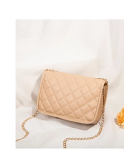 Detail of beige quilted crossbody bag featuring golden chain strap on minimalist background