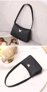 Detail of black quilted shoulder bag featuring a white metal butterfly accent and sleek design