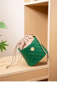 Detail view of green quilted bucket bag with gold chain strap and metal buckle