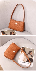 Detail of caramel brown quilted shoulder bag with white butterfly accessory on sofa