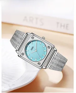 Close-up of square silver steel watch with blue dial resting on white ceramic plate