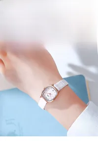 Elegant woman's wrist shot of a square rose gold watch with a white embossed leather strap