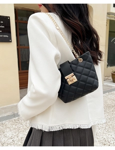 Detail of black quilted crossbody bag with gold chain strap and metal lock closure