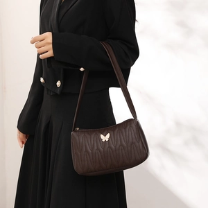Deep brown quilted underarm bag with gold butterfly accent shown on shoulder by model