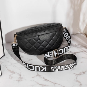 Black quilted crossbody bag with stylish wide strap on marble surface in soft light