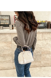 Elegant beige shell handbag with geometric pattern shown in a modern cafe setting