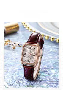 Macro shot of rectangular rose gold watch with crystal dial and burgundy leather strap