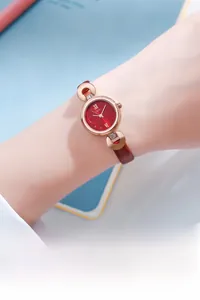 Détail de la montre à cadran rouge, index or rose et bracelet en cuir marron sur le poignet