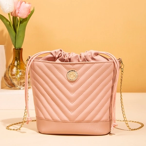 Pink drawstring bucket bag with V-shaped quilting and gold chain strap in a studio setting