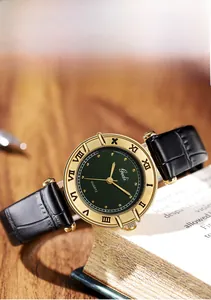 Vintage watch with gold case, green linen dial and black leather strap on old books