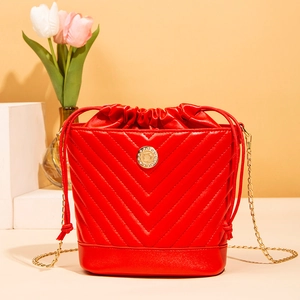 Red quilted bucket bag with golden chain strap and round metal logo on cream base