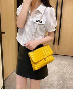 Quilted V-pattern yellow leather crossbody bag with gold chain strap worn by a model