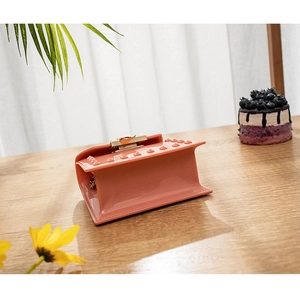 Detail of coral pink jelly bag with gold chain and studs on a wooden surface