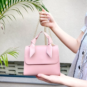 Pink faux leather crossbody bag with chain strap and knotted handle held outdoors