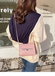 Pink mini crossbody bag featuring a crocodile pattern and a silver bar buckle closure