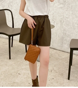 Close-up of a brown quilted diamond pattern clutch bag styled with green leather shorts