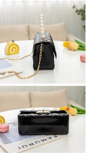Close-up of black quilted lacquer handbag featuring a pearl handle and gold chain strap