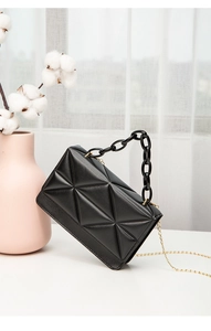 Detail of black quilted shoulder bag with resin chain and gold metal strap