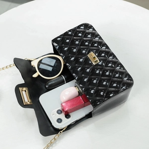 Black quilted jelly crossbody bag with gold chain and interior items on white surface