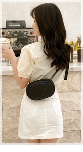 Détail d'un sac ceinture noir matelassé à motif chevron porté par un mannequin